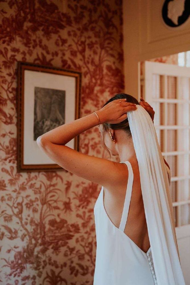 The bride adjusts her veil against the Toile de Jouy wallpaper