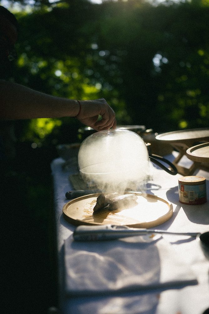The caterer lifts a smoking cloche