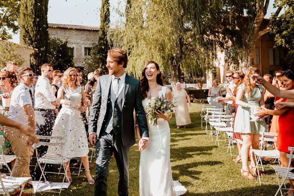 The newlyweds leave the ceremony under confetti, surrounded by their guests