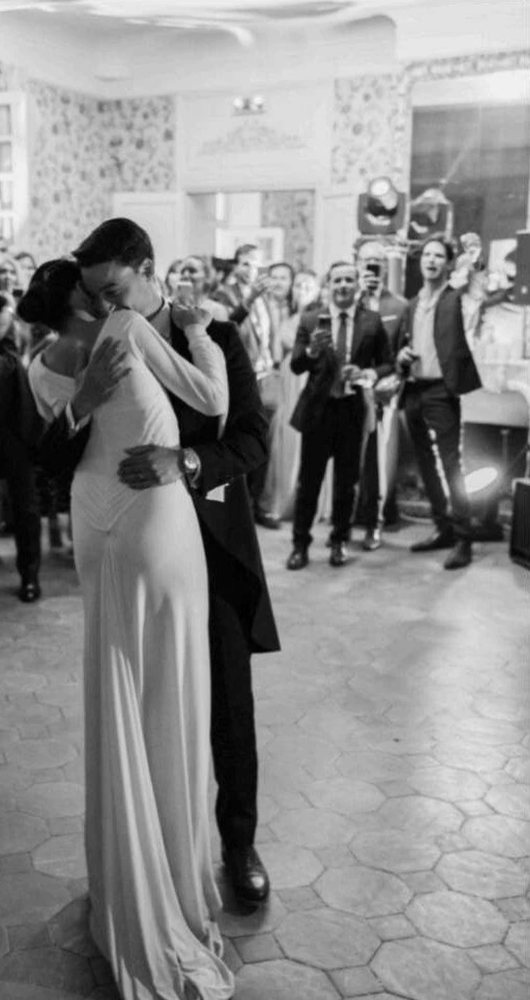 The newlyweds embrace on the salon dance floor, guests all around