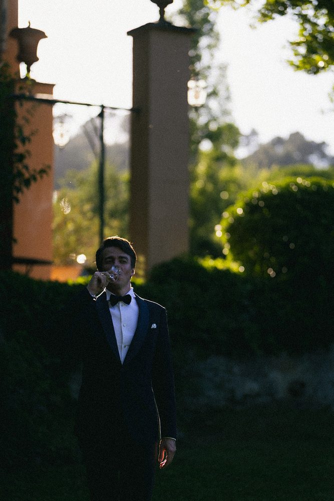 The groom raises his glass before the garden pillars
